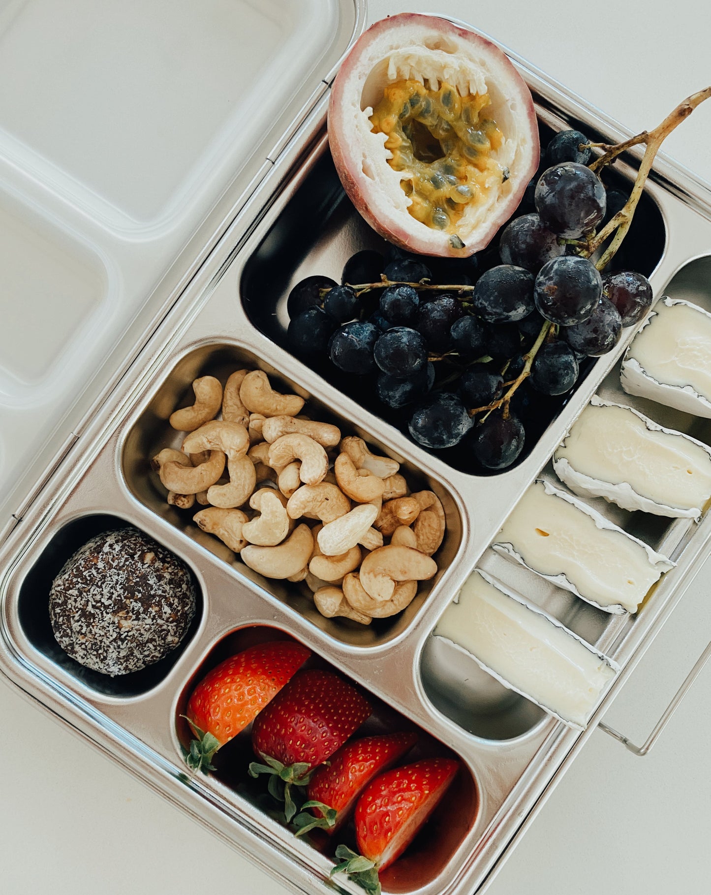 Stainless steel bento box with 5 compartments. Sustainable, eco-friendly, and zero plastic lunchbox alternative. Fruit, soft-cheese cashew nuts, and raw treats - ready for the perfect picnic.